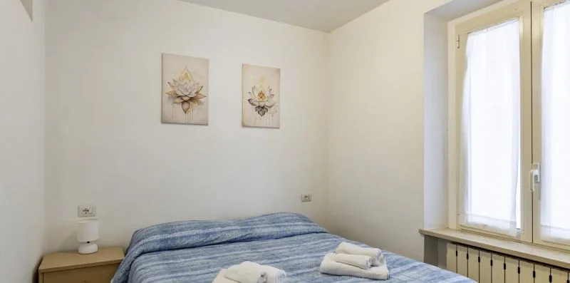 Un dormitorio con una cama bajo dos cuadros florales y una ventana luminosa.
