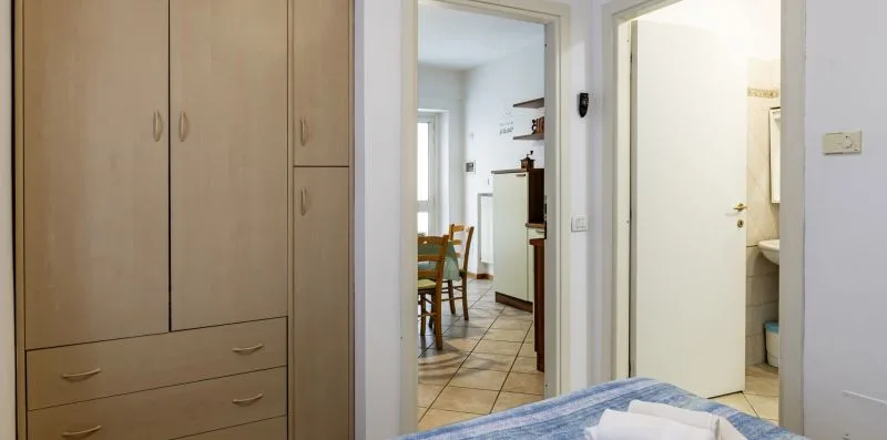 A bedroom with built-in wardrobes and a view through an open doorway to a dining area.