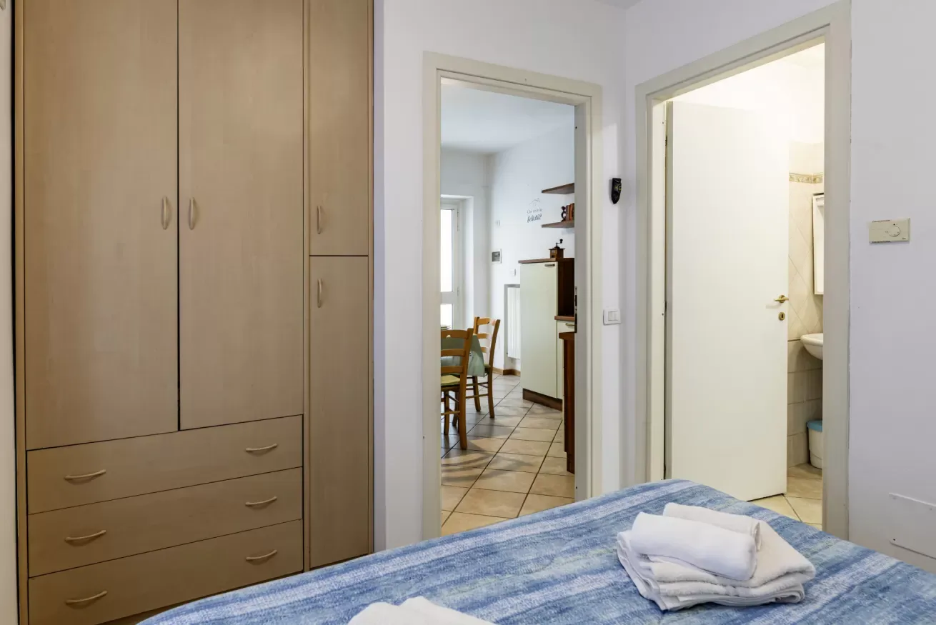 A bedroom with a large built-in wardrobe and an open doorway to a dining area.