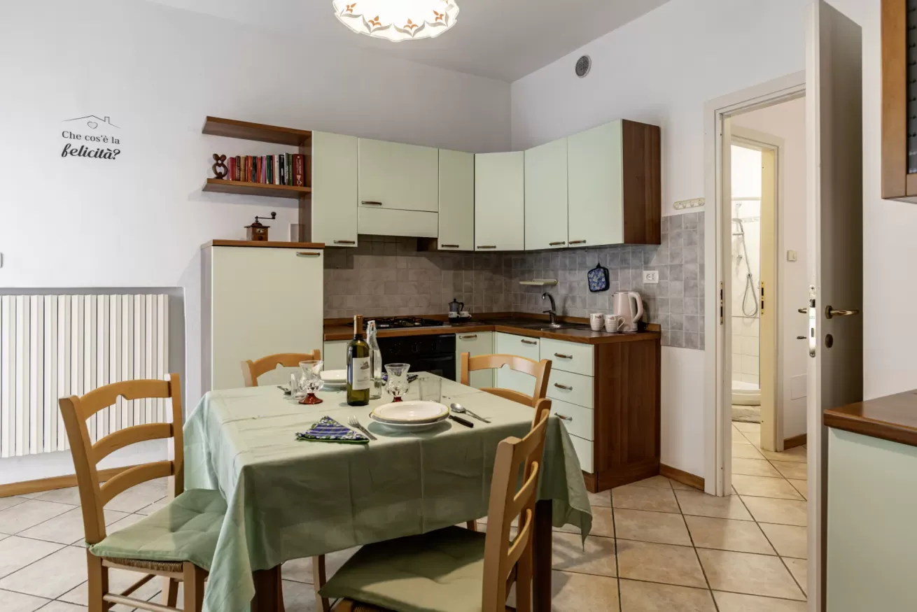 A dining area with a table in front of a compact kitchen.
