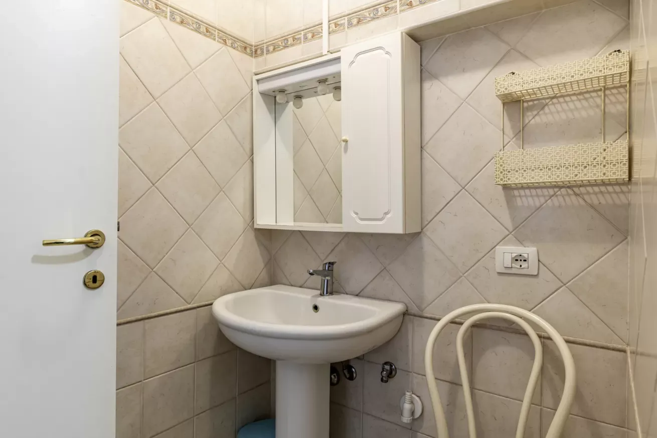 A tiled bathroom with a pedestal sink and mirrored wall cabinet.