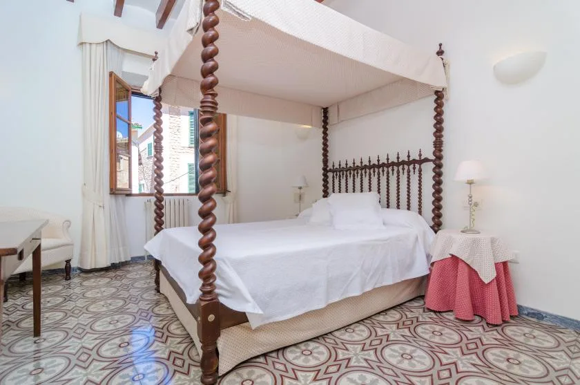 A bedroom with a white bed, tall wooden bedposts, and patterned floor tiles.