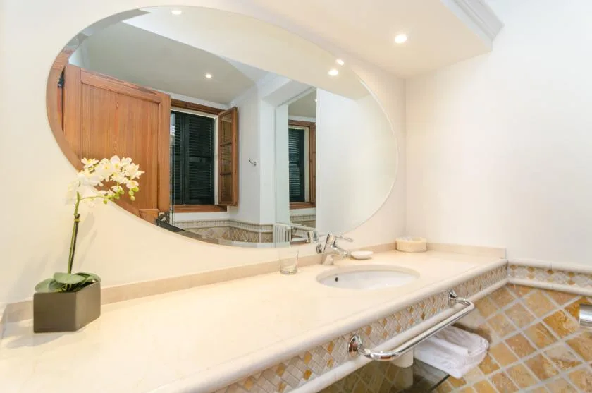 A bathroom vanity with a wide oval mirror and a flower arrangement.