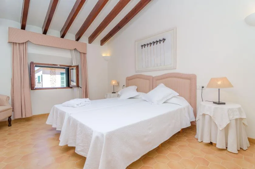 A bedroom with a large bed, pale bedding, and exposed ceiling beams.