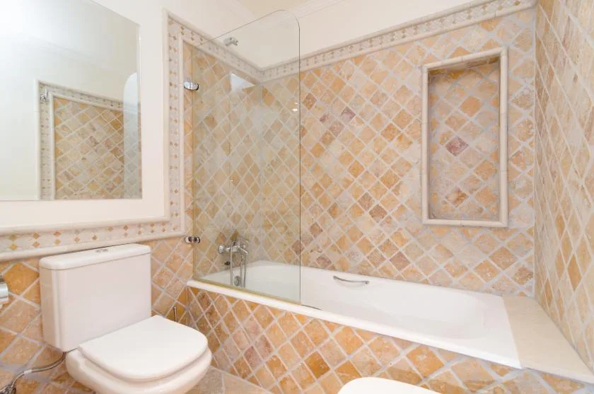 A tiled bathroom with a bathtub, glass screen, and toilet.