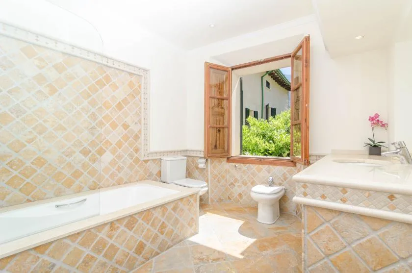 A bright tiled bathroom with a bathtub, sink, and open window.