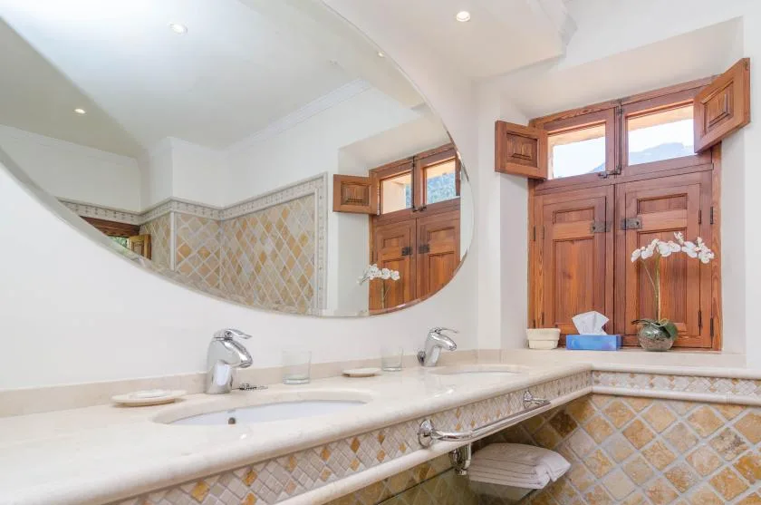 A bathroom vanity with a wide mirror and wooden window shutters.