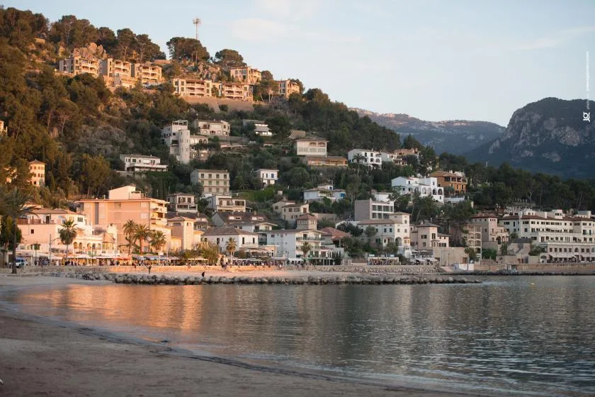 A coastal town stretches along the water beneath a wooded hillside.