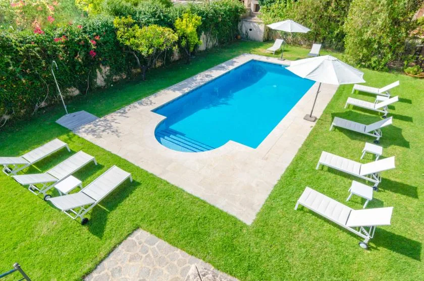 An outdoor swimming pool is surrounded by a lawn, loungers, and umbrellas.