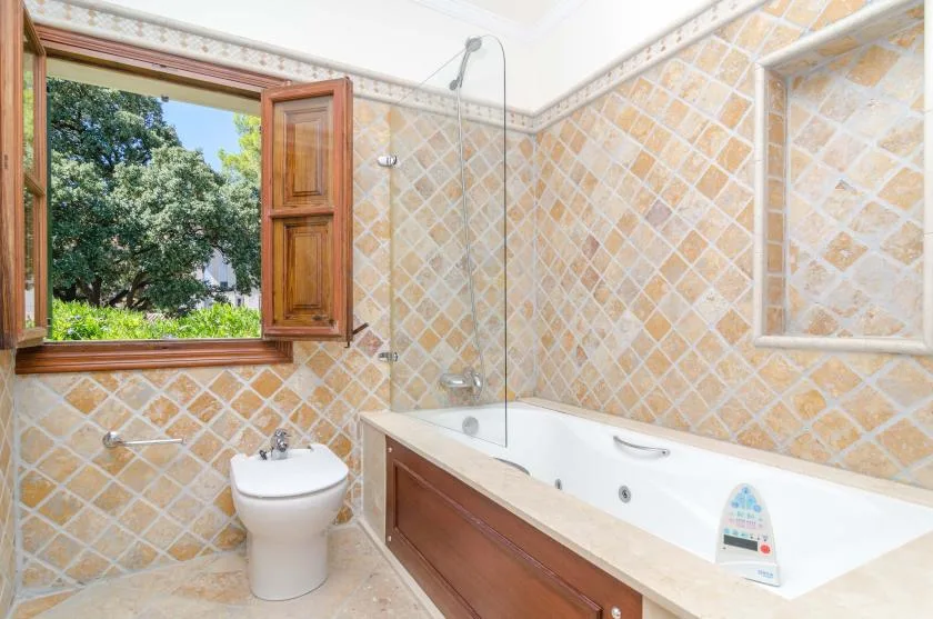 A tiled bathroom with a bathtub, sink, and open window.