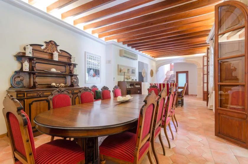 A dining room with a long wooden table, red chairs, and exposed ceiling beams.