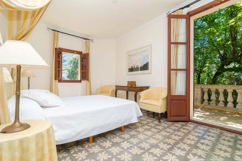 A bedroom with a bed, armchair, and open glass doors overlooking leafy greenery.
