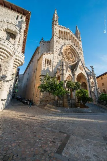 A stone Gothic church with a large rose window stands beside a cobbled street.
