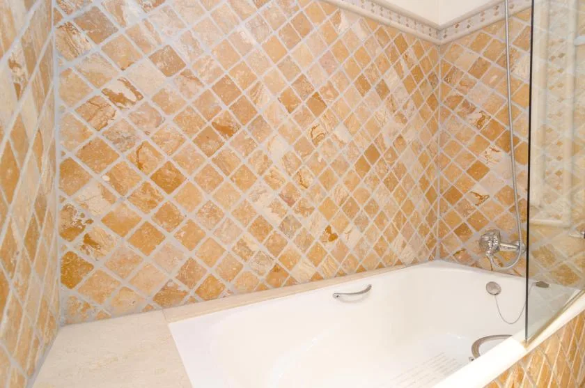 A tiled bathroom shows a bathtub with a handheld shower.