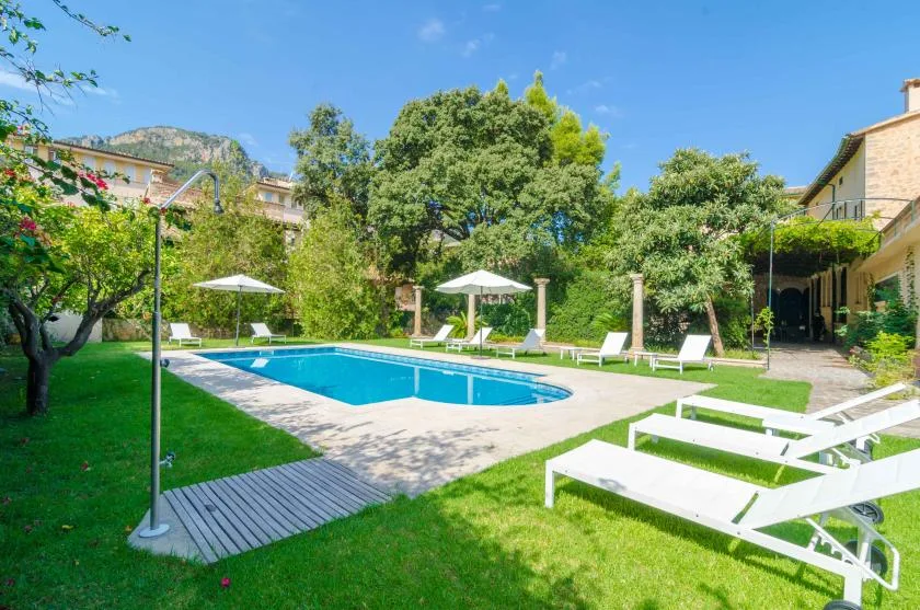 An outdoor swimming pool sits in a landscaped garden with white loungers.