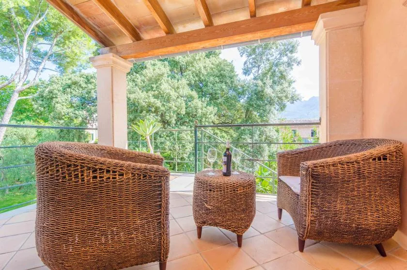 A covered outdoor seating area with woven furniture overlooks leafy trees.