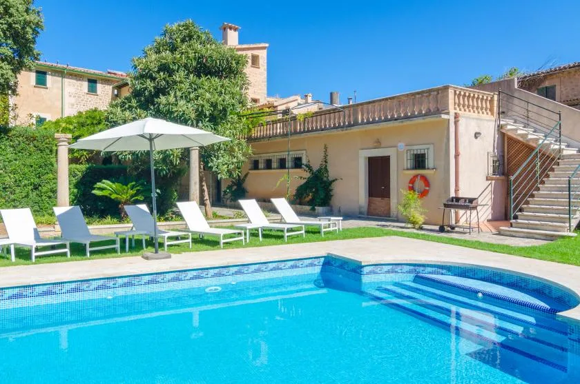 An outdoor swimming pool is bordered by lounge seating and a white parasol.