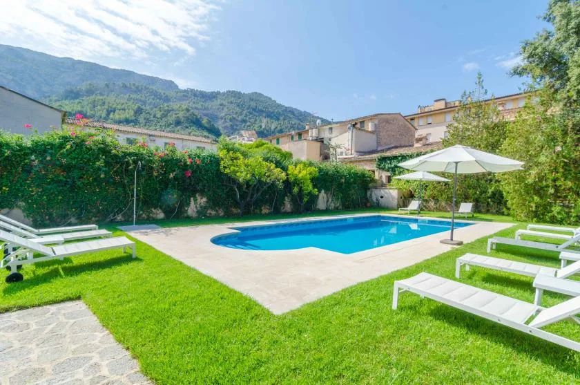 An outdoor swimming pool sits in a grassy courtyard with lounge chairs and an umbrella.