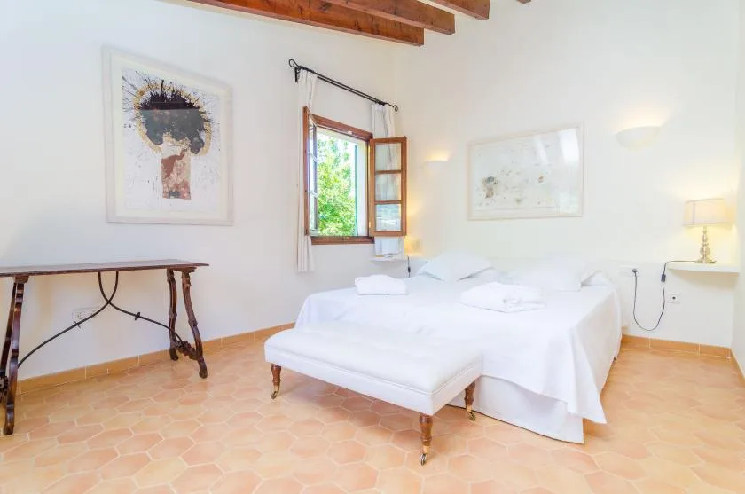A bright bedroom with a white bed, an open window, and framed artwork.