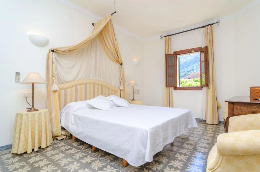 A bedroom with a large bed beneath a draped canopy and an open window.