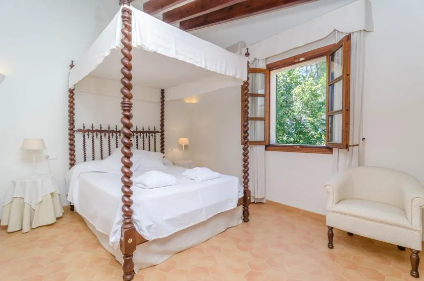 A bedroom with a canopy bed and an open window overlooking greenery.