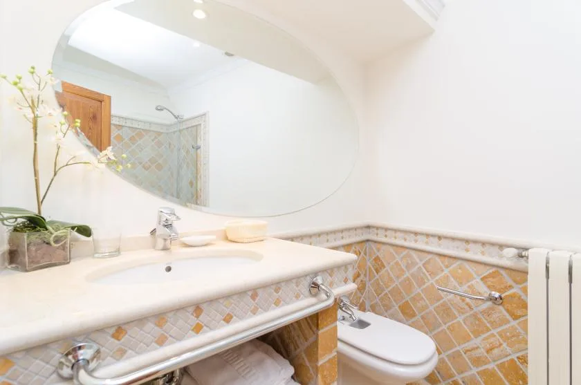 A bright bathroom with a sink, large mirror, and tiled walls.