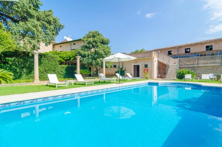 An outdoor swimming pool beside a landscaped patio with lounge seating.