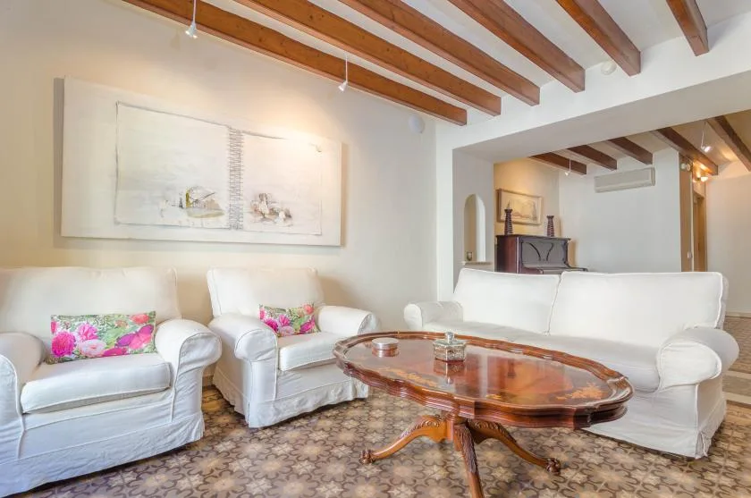 A bright living room with white seating and a wooden coffee table beneath exposed ceiling beams.