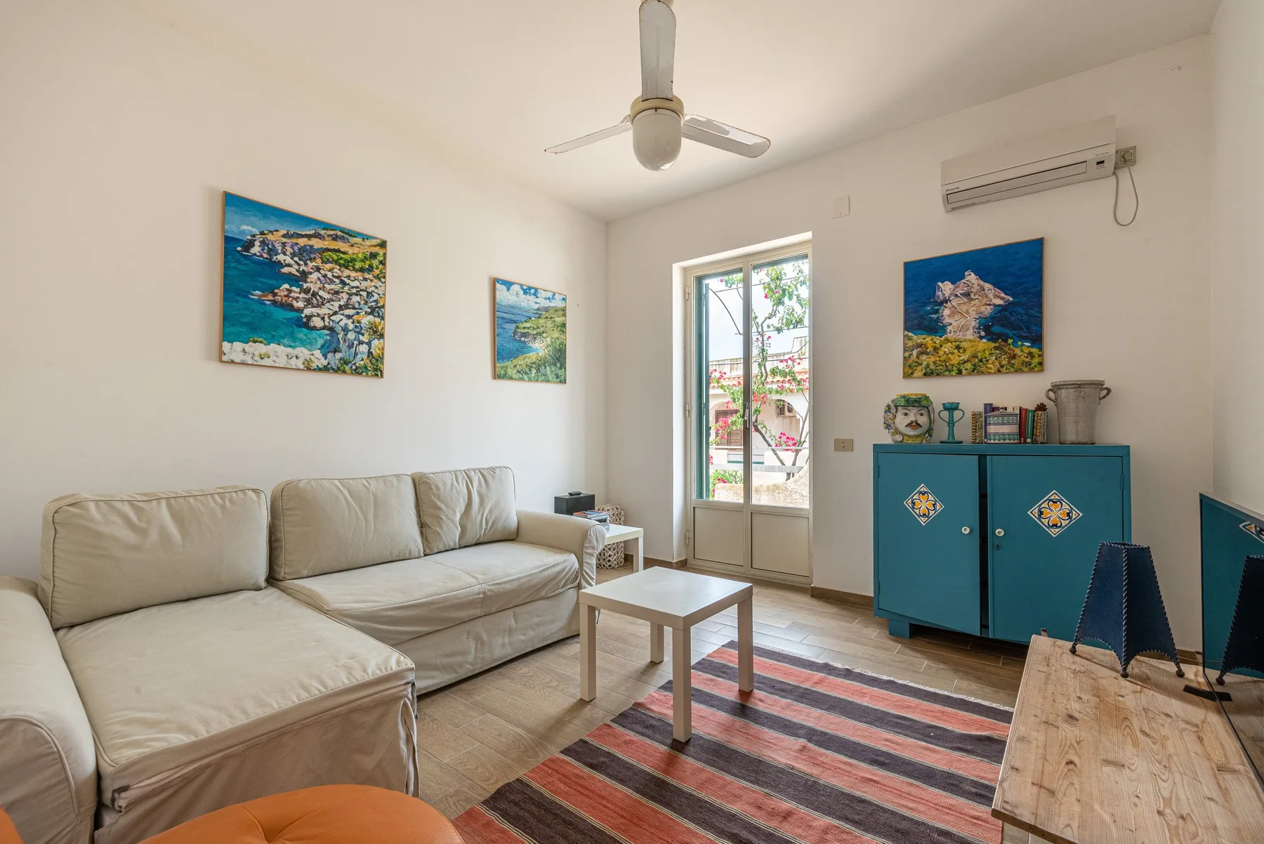 A bright living room with light seating, a small table, and colorful artwork.