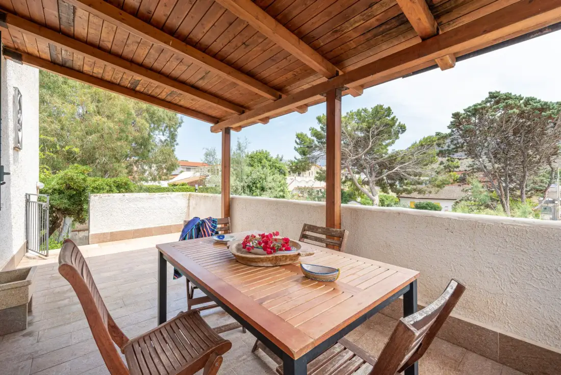 A covered outdoor dining area with a wooden table and surrounding greenery.
