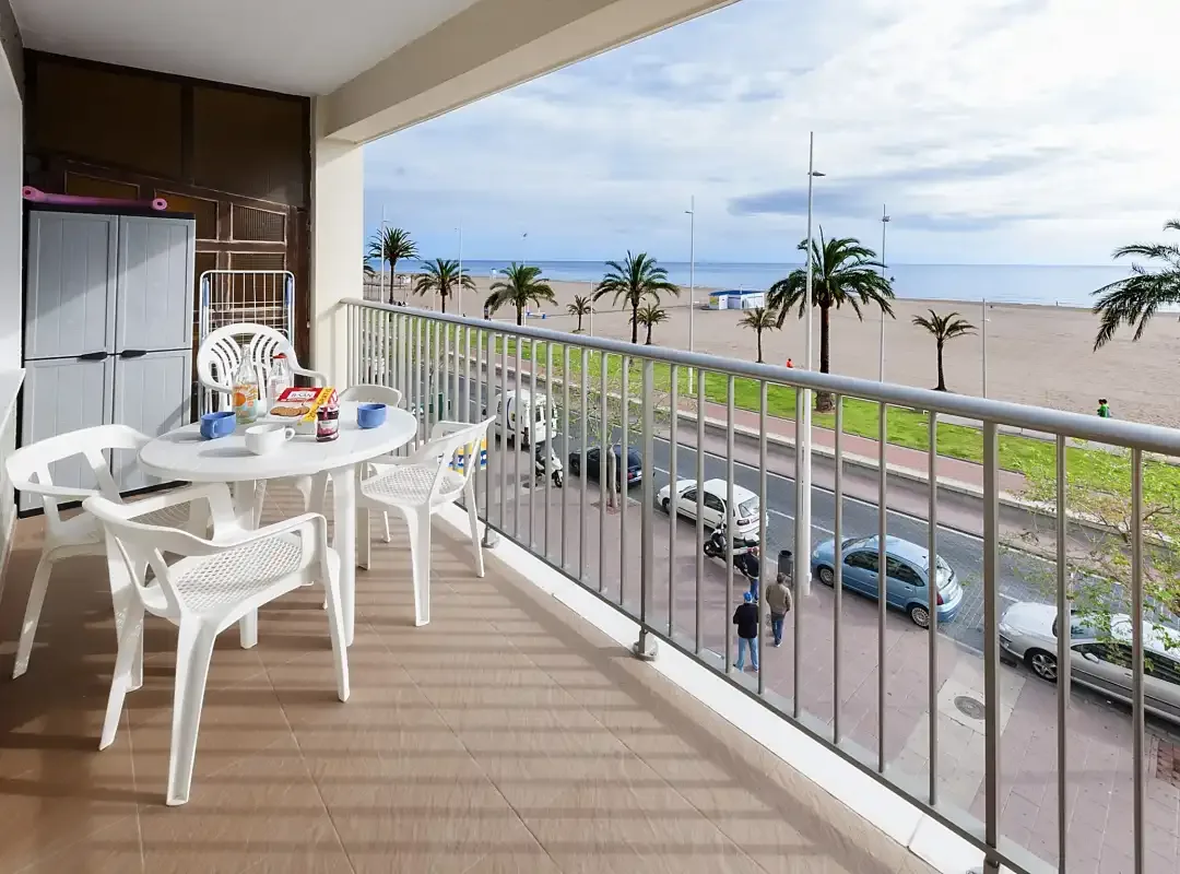 Una zona de comedor en el balcón da a una playa bordeada de palmeras y al mar.