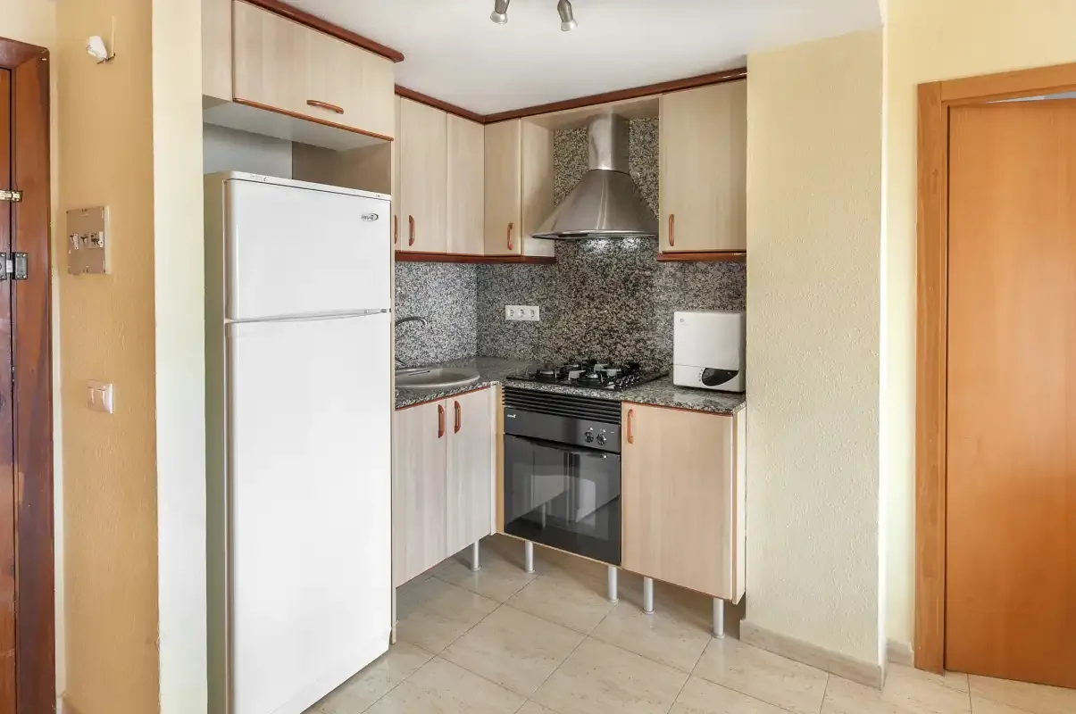 A compact kitchen with light cabinetry, a refrigerator, and a built-in oven.