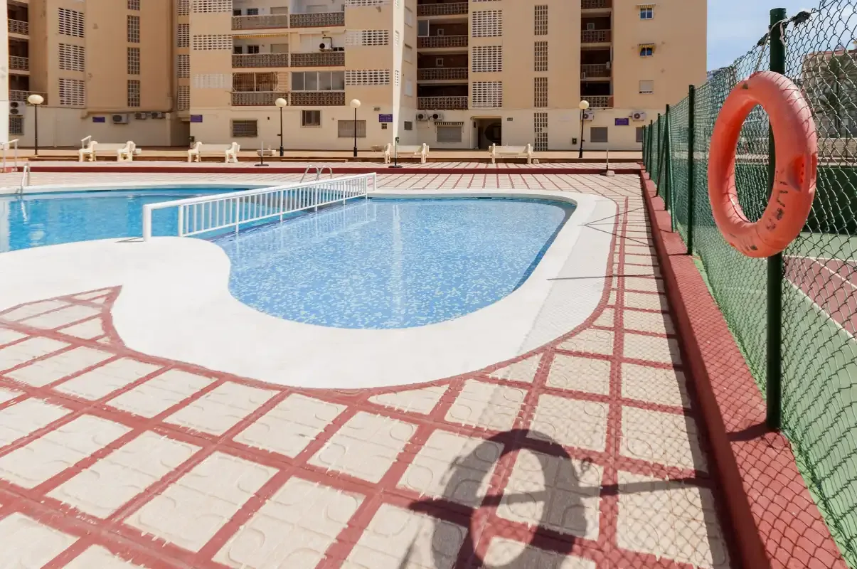 Una piscina al aire libre junto a una terraza vallada y edificios de apartamentos.