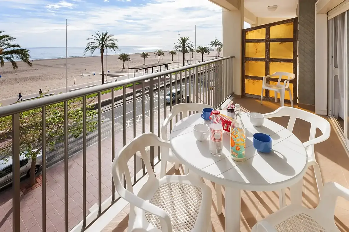 Una zona de comedor en el balcón da a una playa con palmeras y al mar.