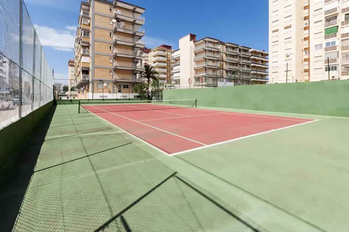 An outdoor tennis court with apartment buildings in the background.