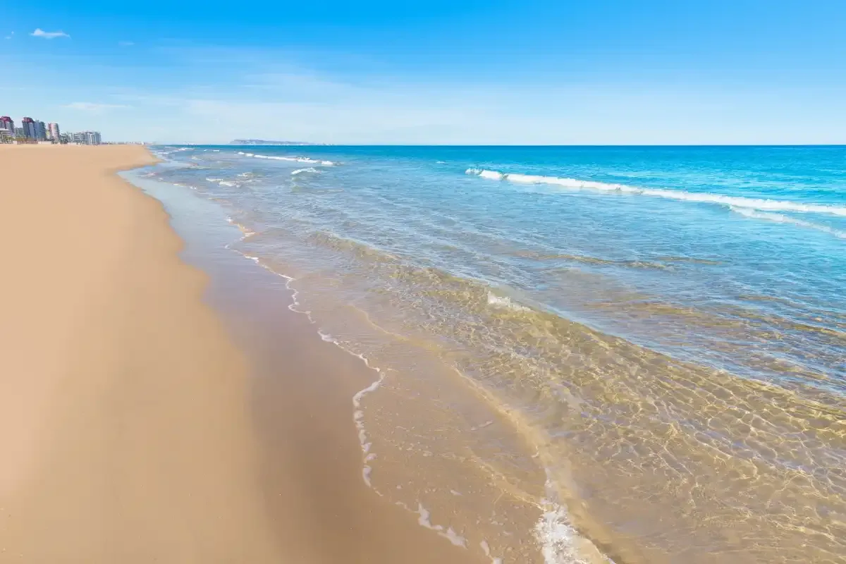 A sandy beach stretches alongside clear blue water under a bright sky.