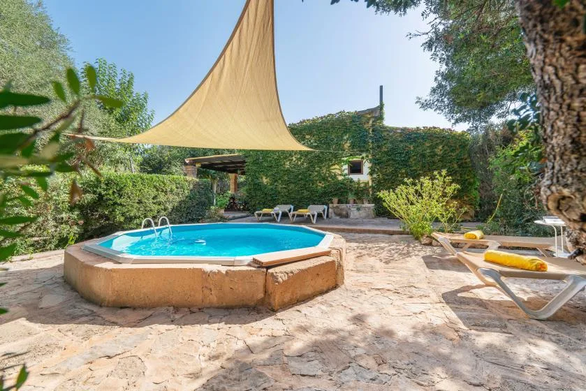 Una piscina al aire libre está bajo una vela de sombra triangular en un jardín frondoso.
