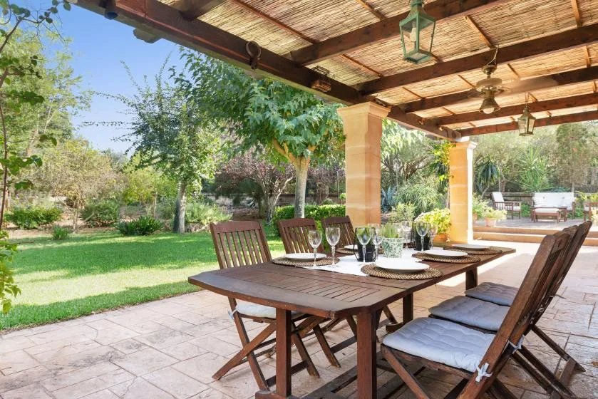 Una zona de comedor al aire libre cubierta, con una mesa de madera y vistas al jardín.
