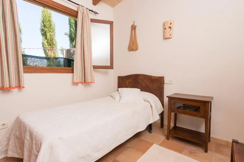 Un dormitorio con una cama individual junto a una mesita de madera y una ventana.