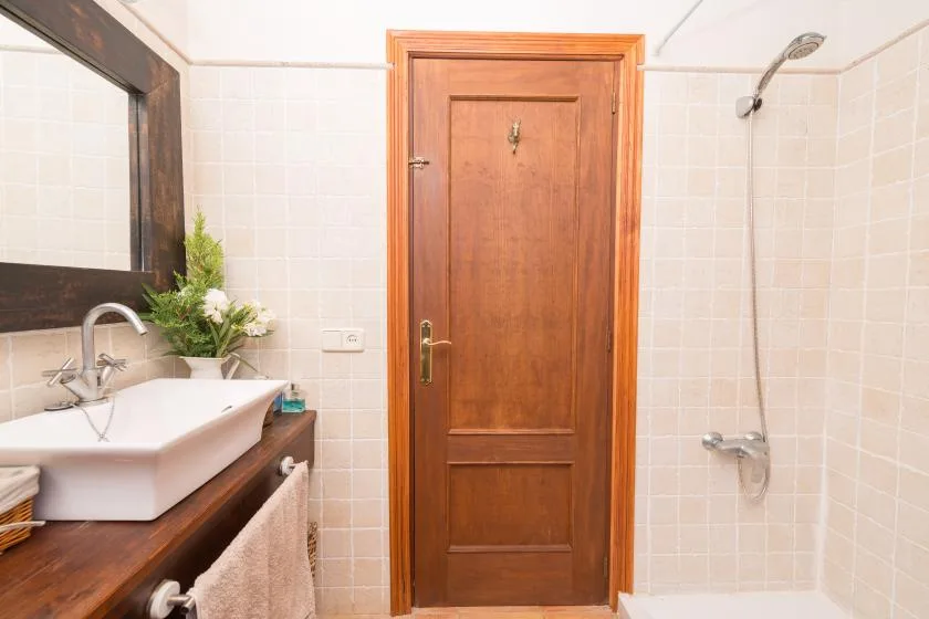 Un baño alicatado con lavabo, espejo y una puerta de madera.