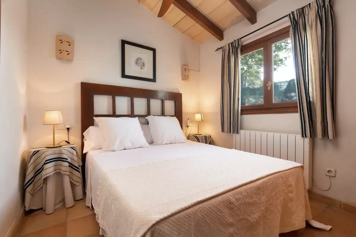Un dormitorio con una cama doble bajo un techo inclinado con vigas de madera.