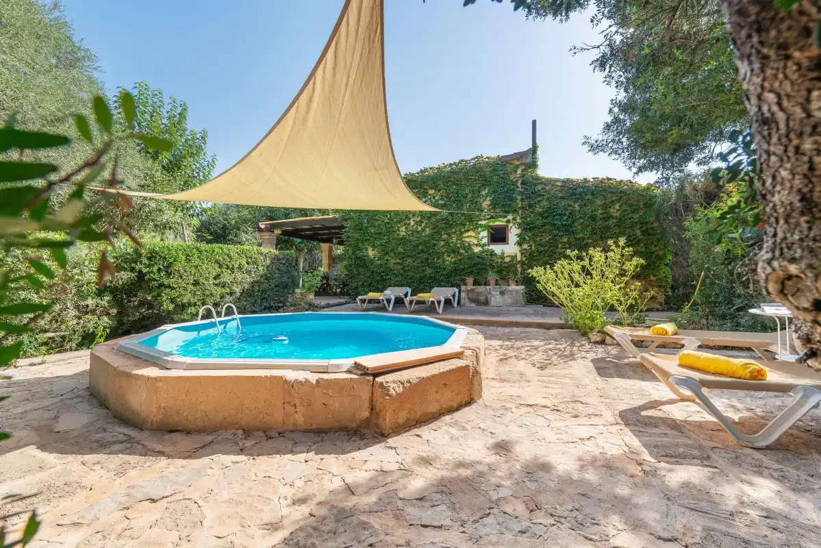 Un patio ajardinado con una piscina pequeña y asientos a la sombra.