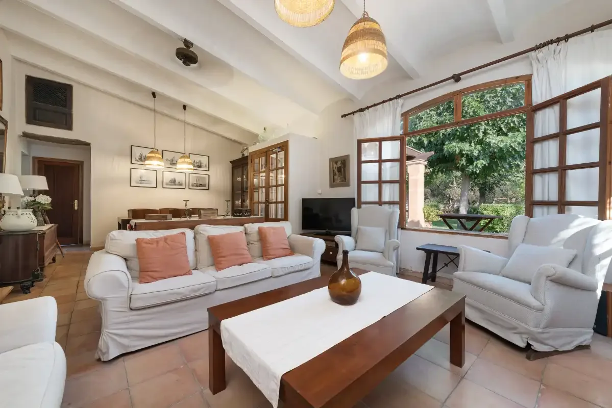 Sala de estar con asientos alrededor de una mesa de centro junto a ventanas abiertas.