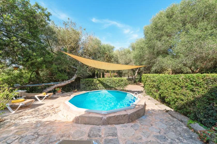 Una piscina al aire libre está en un patio de piedra bajo una vela de sombra.