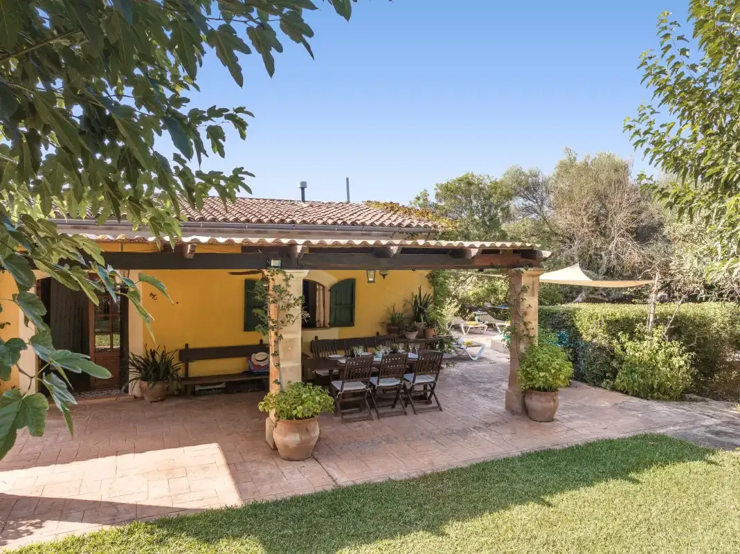 Una casa amarilla da a un patio sombreado con asientos al aire libre.