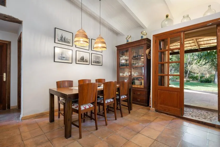 Comedor con mesa de madera, sillas y armario con puertas de cristal.