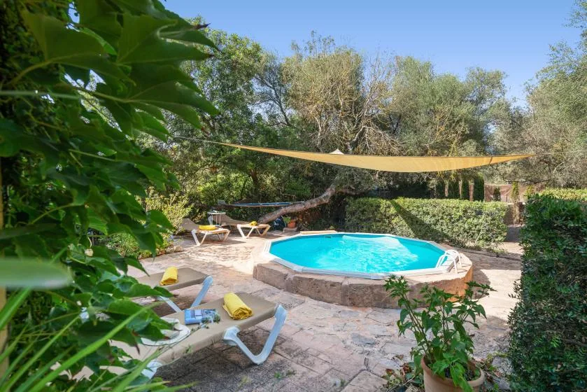 Una piscina al aire libre está en un jardín pavimentado con tumbonas y árboles frondosos.