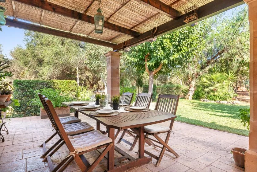 Comedor exterior cubierto con una mesa de madera y vistas al jardín.