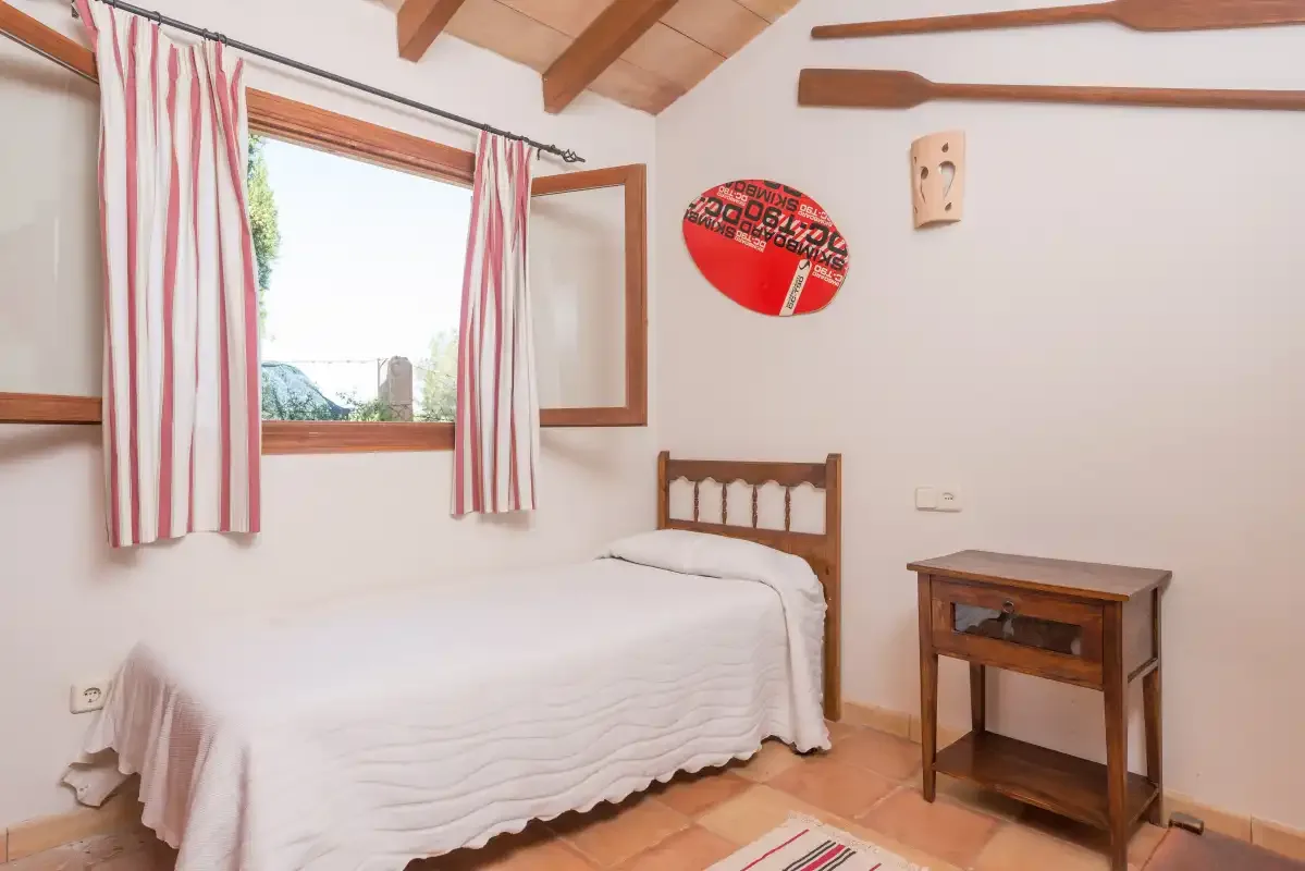 Un dormitorio con una cama individual, cortinas a rayas y una mesita de madera.