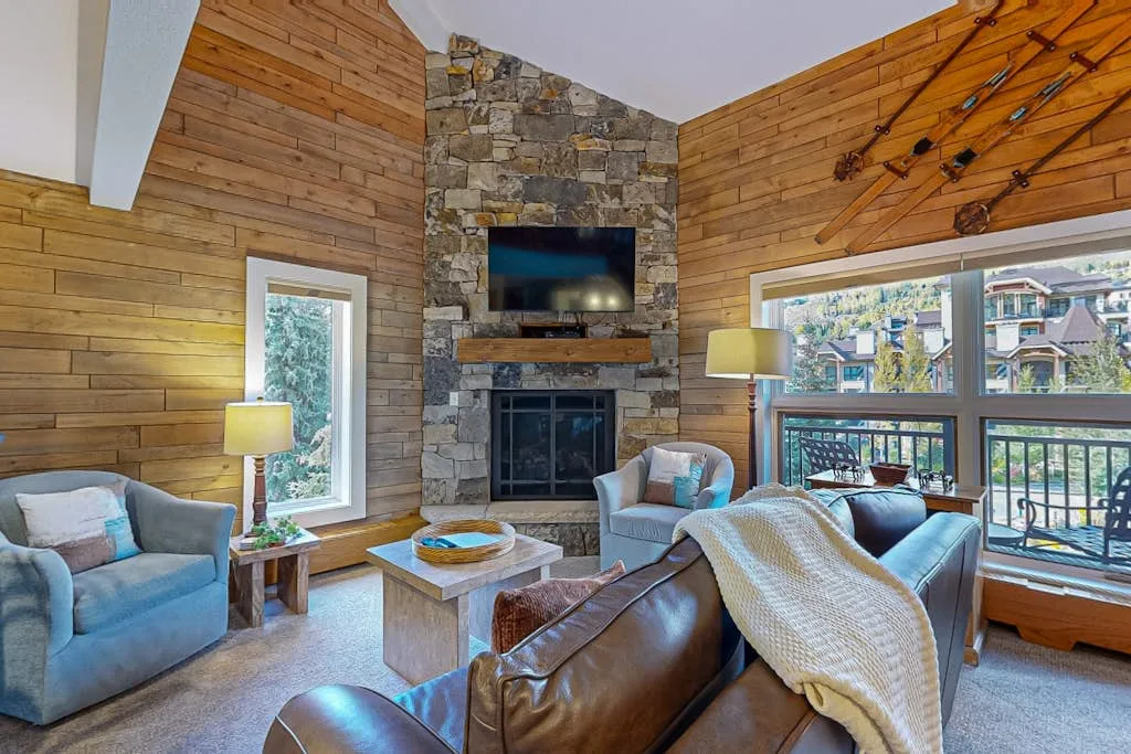 A living room with wood-paneled walls, a stone fireplace, and seating.